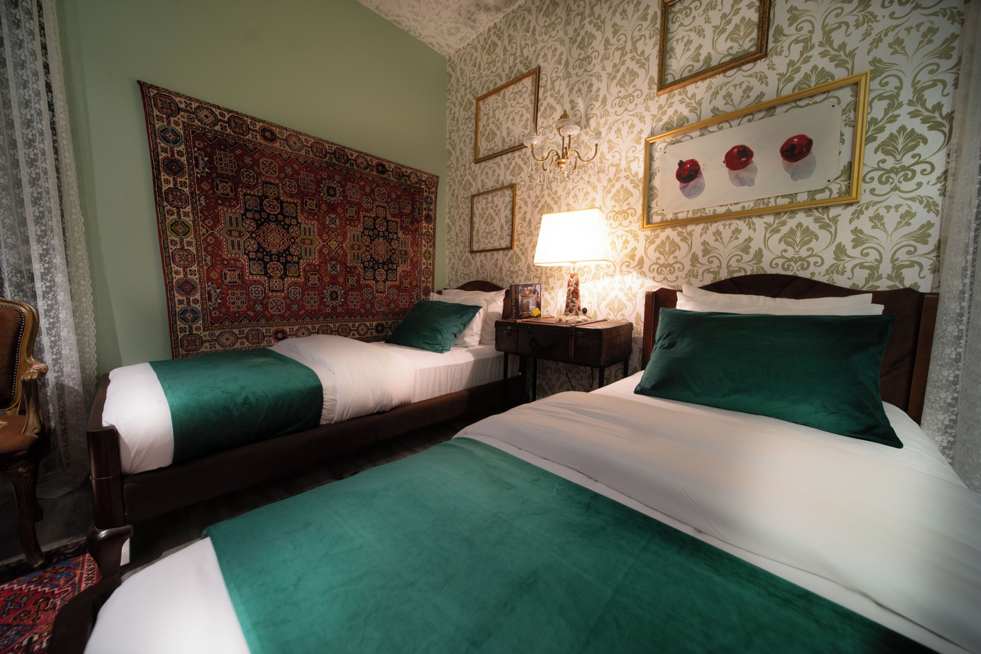 Habitación de hotel con dos camas, un tapete grande de estampado llamativo, una lámpara de pared y cuadros enmarcados.