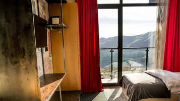 Un dormitorio con una ventana grande, una cama, un escritorio y vistas al exterior.