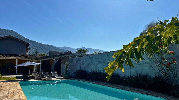 Une piscine entourée d’un petit muret et de verdure, avec des chaises longues et des parasols.
