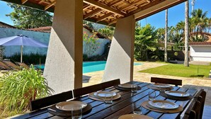 Un espace de restauration en plein air avec des tables et des chaises en bois, une piscine en arrière-plan et des palmiers.