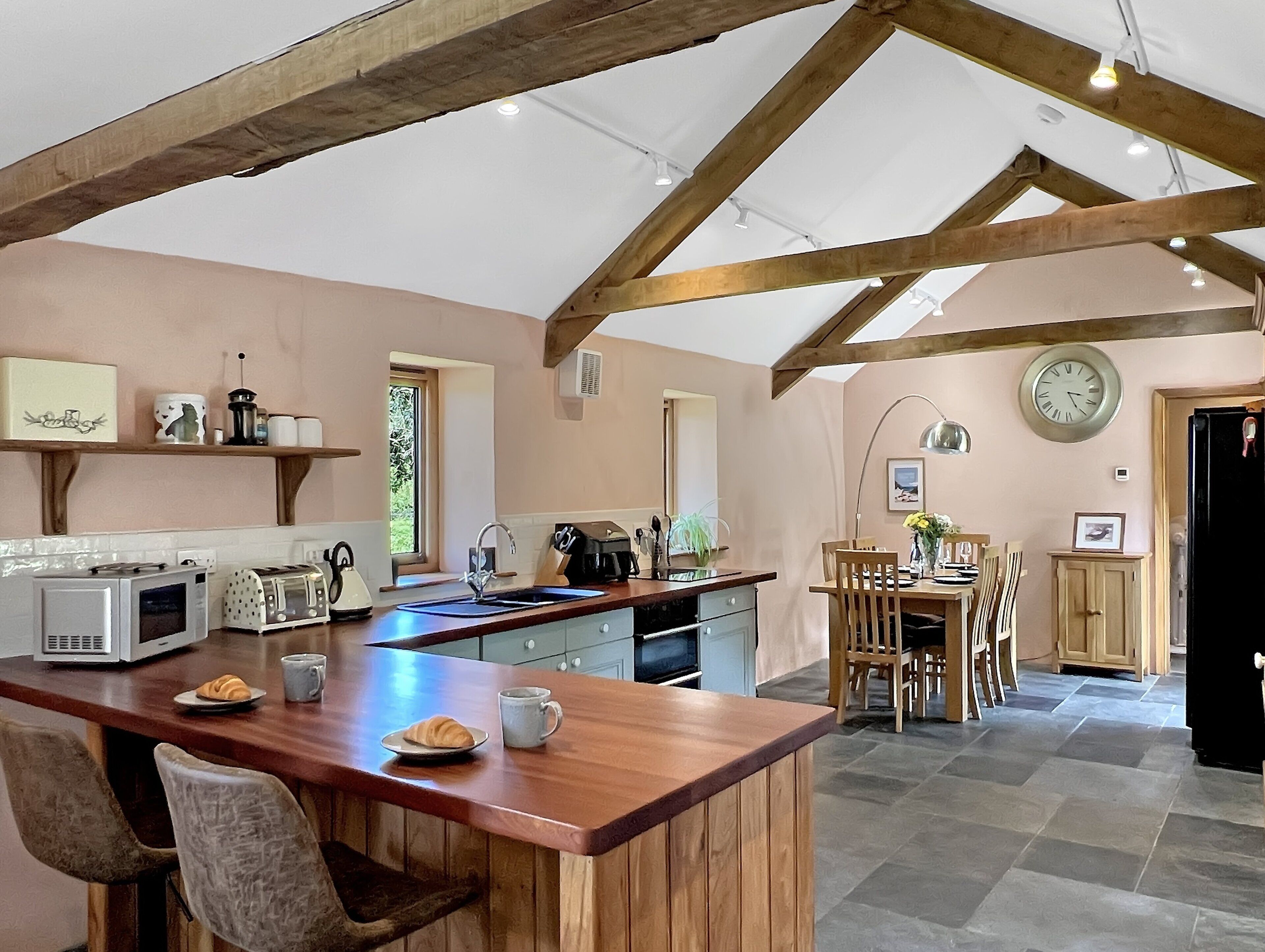Una cucina con isola in legno, un'area pranzo con sedie, un orologio e una finestra.