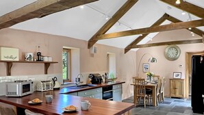 Een keuken met een houten eiland, een eethoek met stoelen, een klok en een raam.