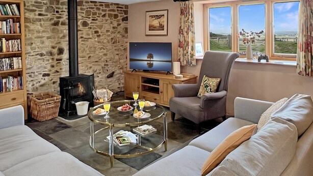 Een gezellige woonkamer met een stenen muur, een open haard, een televisie, een comfortabele bank en een groot raam met uitzicht.