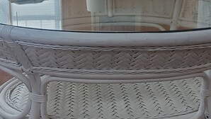 Une pièce comprenant un canapé en osier, une table basse avec un plateau en verre et deux fauteuils. Une lampe se trouve sur une petite table placée à côté des fauteuils.