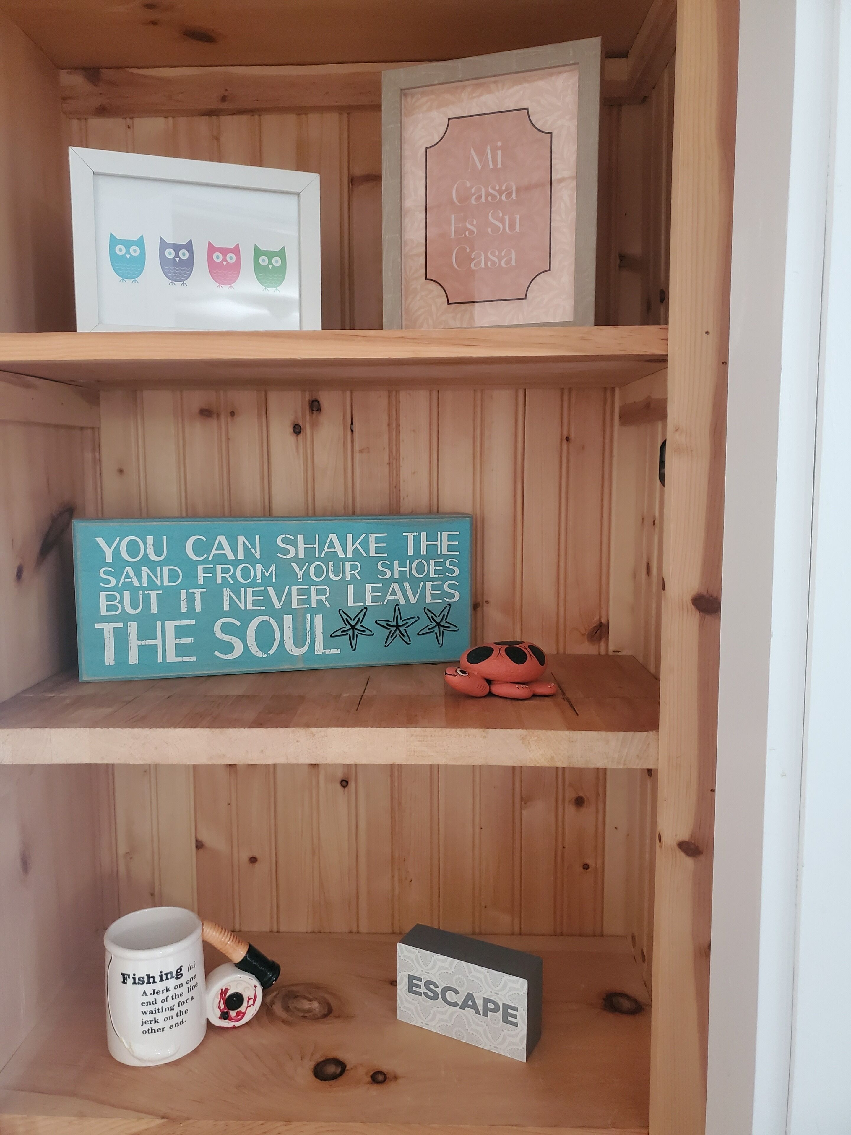 Ein Holzregal mit verschiedenen Gegenständen, darunter ein gerahmtes Bild von Eulen, ein Schild mit einem Zitat, eine Tasse und eine kleine Schachtel.
