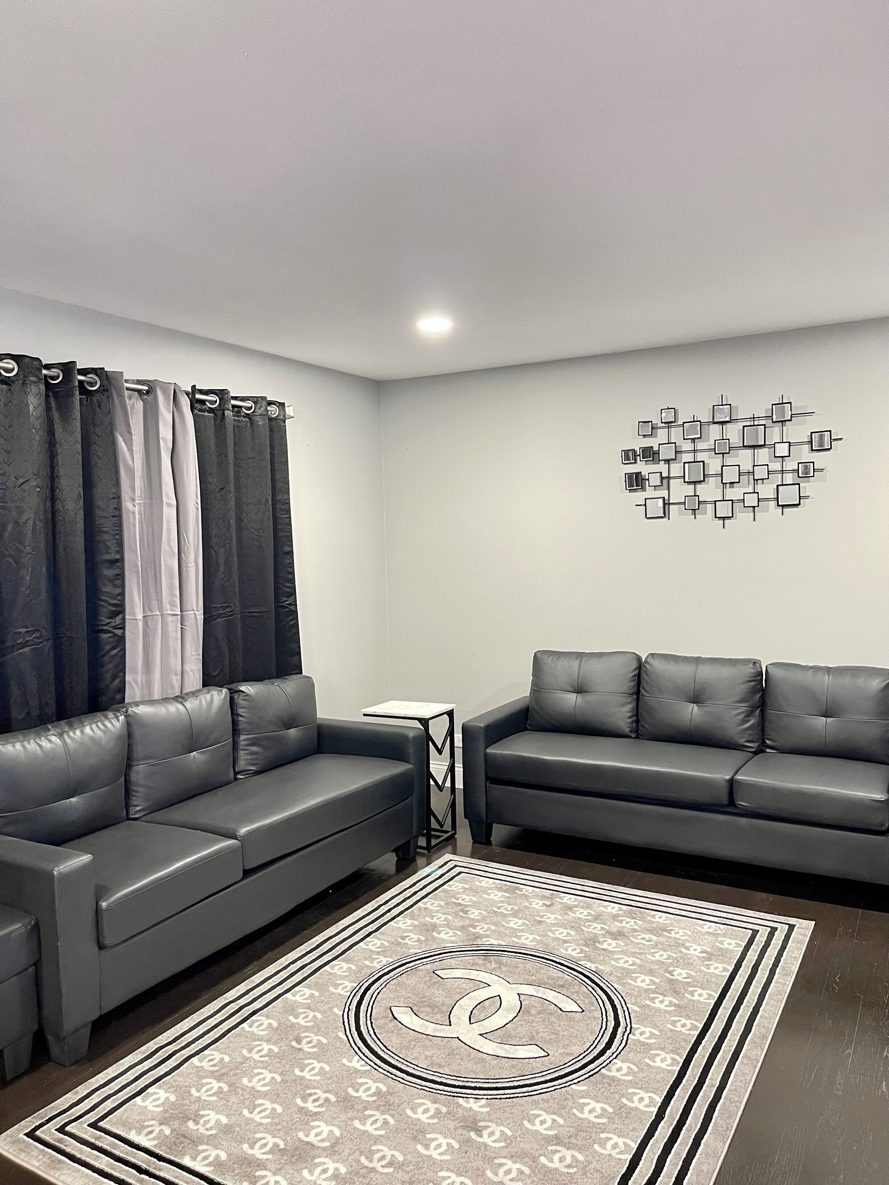 Una sala de estar moderna con dos sofás de cuero gris, un tapete estampado y una obra de arte en la pared.