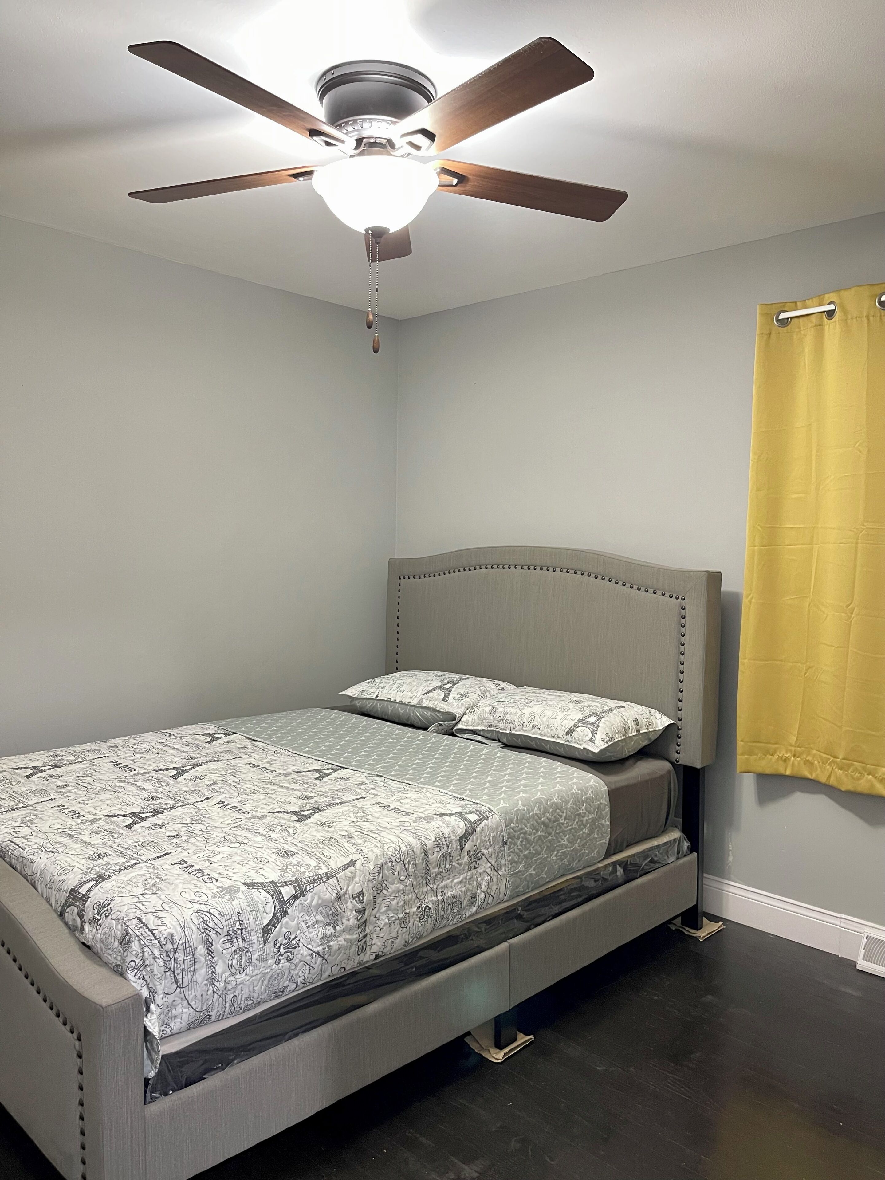 A bedroom with a bed, a ceiling fan, and a yellow curtain.