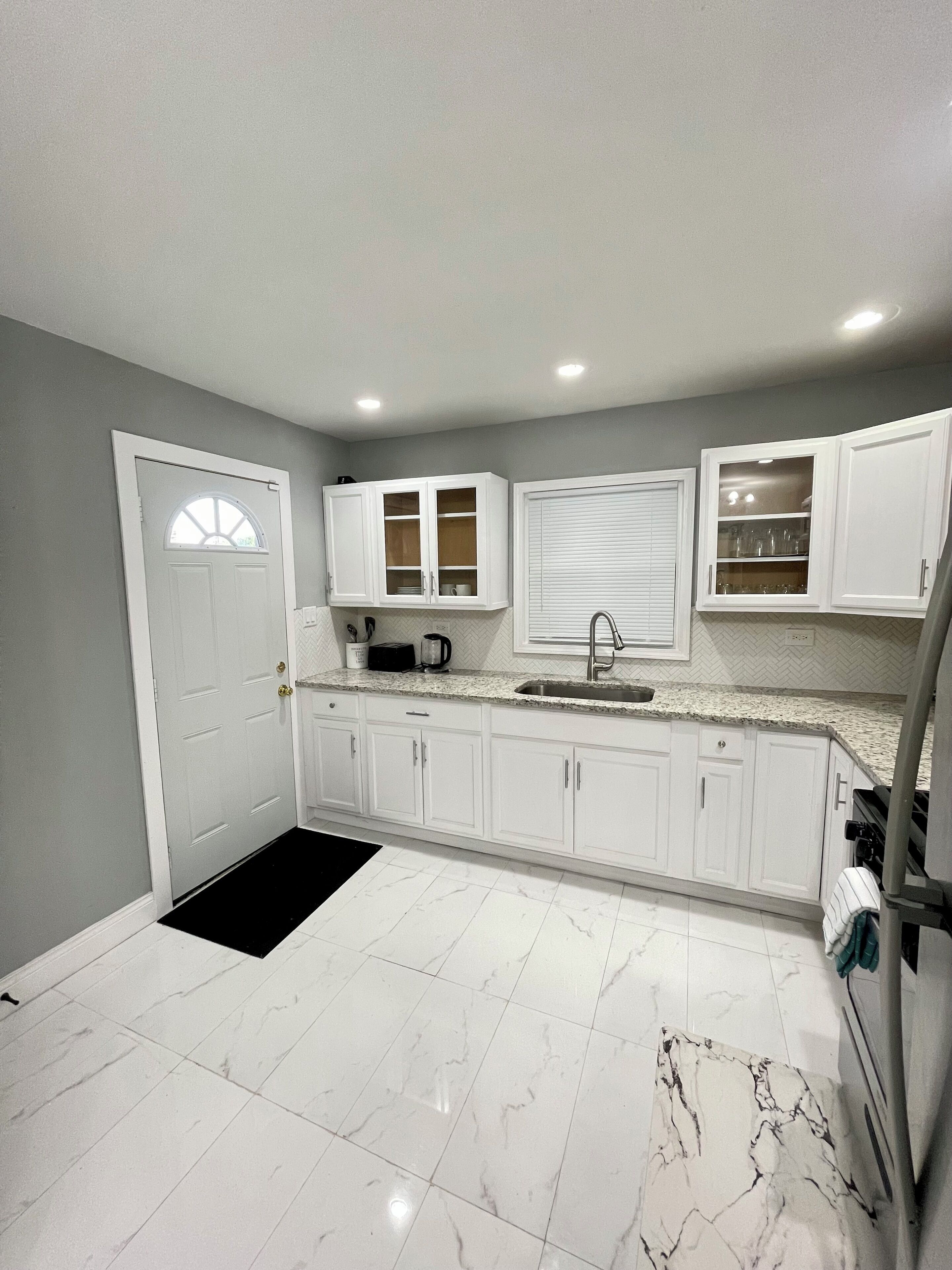 Una cocina con gabinetes blancos, un felpudo negro y una puerta blanca con ventanal.