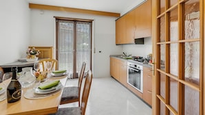 A modern kitchen with wooden cabinets, a dining area with a table set for four, and a sliding glass door leading to a balcony. - The Olive Tree Garden With Mountain View, Arco, Italy (Arco)