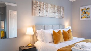 Een hotelkamer met een bed, nachtkastje, lamp, schilderij en een ingelijste foto aan de muur.