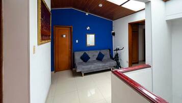 Quarto com parede azul, sofá cinza, porta de madeira e uma bicicleta.