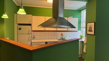 A kitchen with green walls, white cabinets, and a wooden countertop. There is a stainless steel range hood above the stove, and pendant lights hanging above.