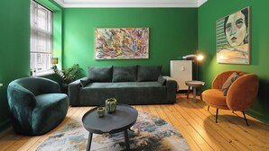 Sala de estar com parede verde, sofá cinza, poltrona azul-turquesa, mesa de centro redonda e poltrona laranja pequena.