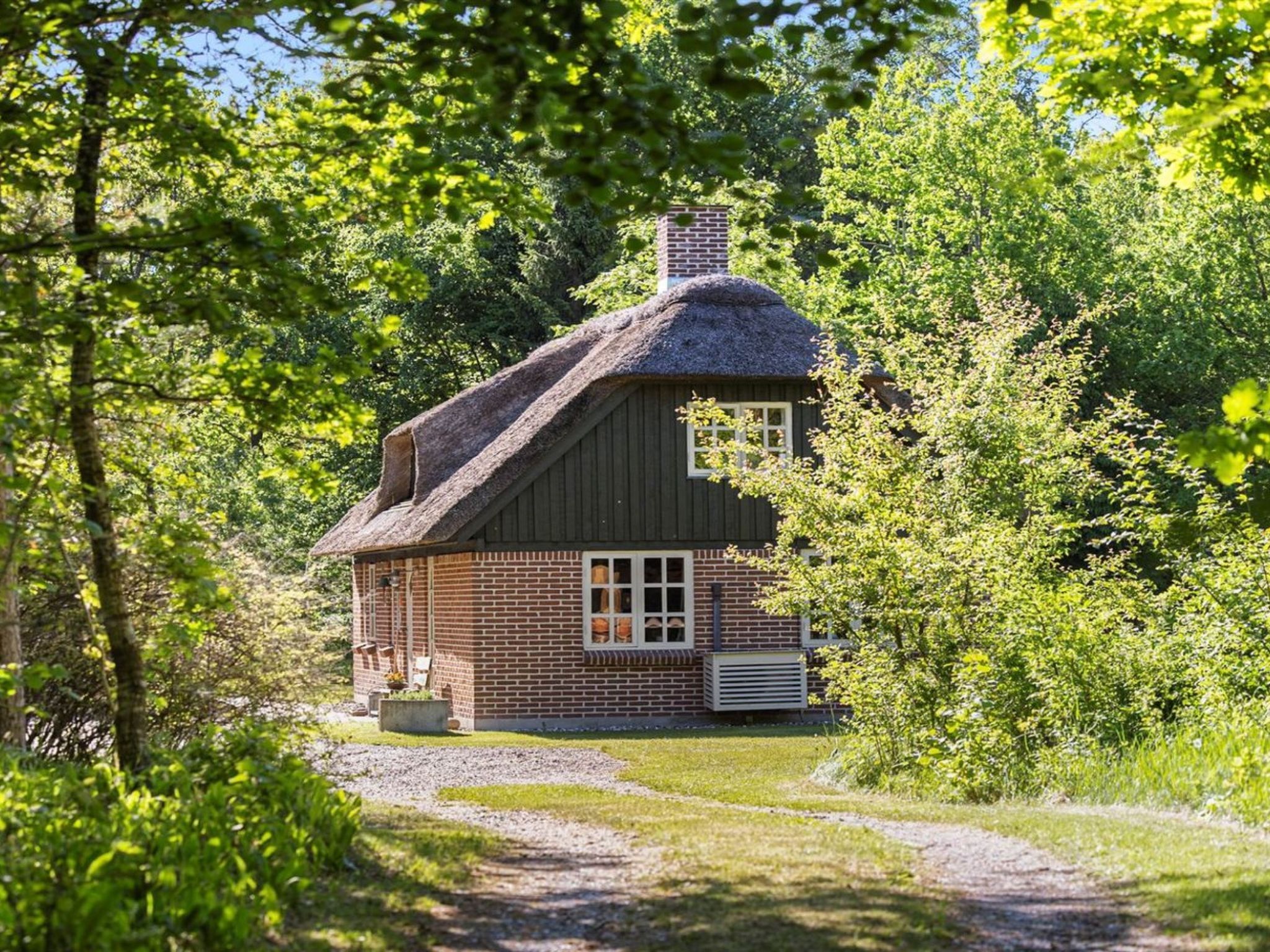 Ein traditionelles Backsteinhaus mit Strohdach, umgeben von üppiger Vegetation und einem Kiesweg.