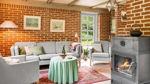 Ein gemütliches Wohnzimmer mit Backsteinwand, Kamin, einer Couch, einem Tisch und einer Hängelampe.