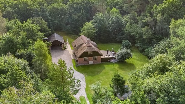 Ein Haus, umgeben von dichtem Wald, mit einem gepflegten Rasen und einem Schotterweg.