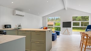 A modern kitchen with a large island, a dining area with wooden chairs, and a TV on a stand.