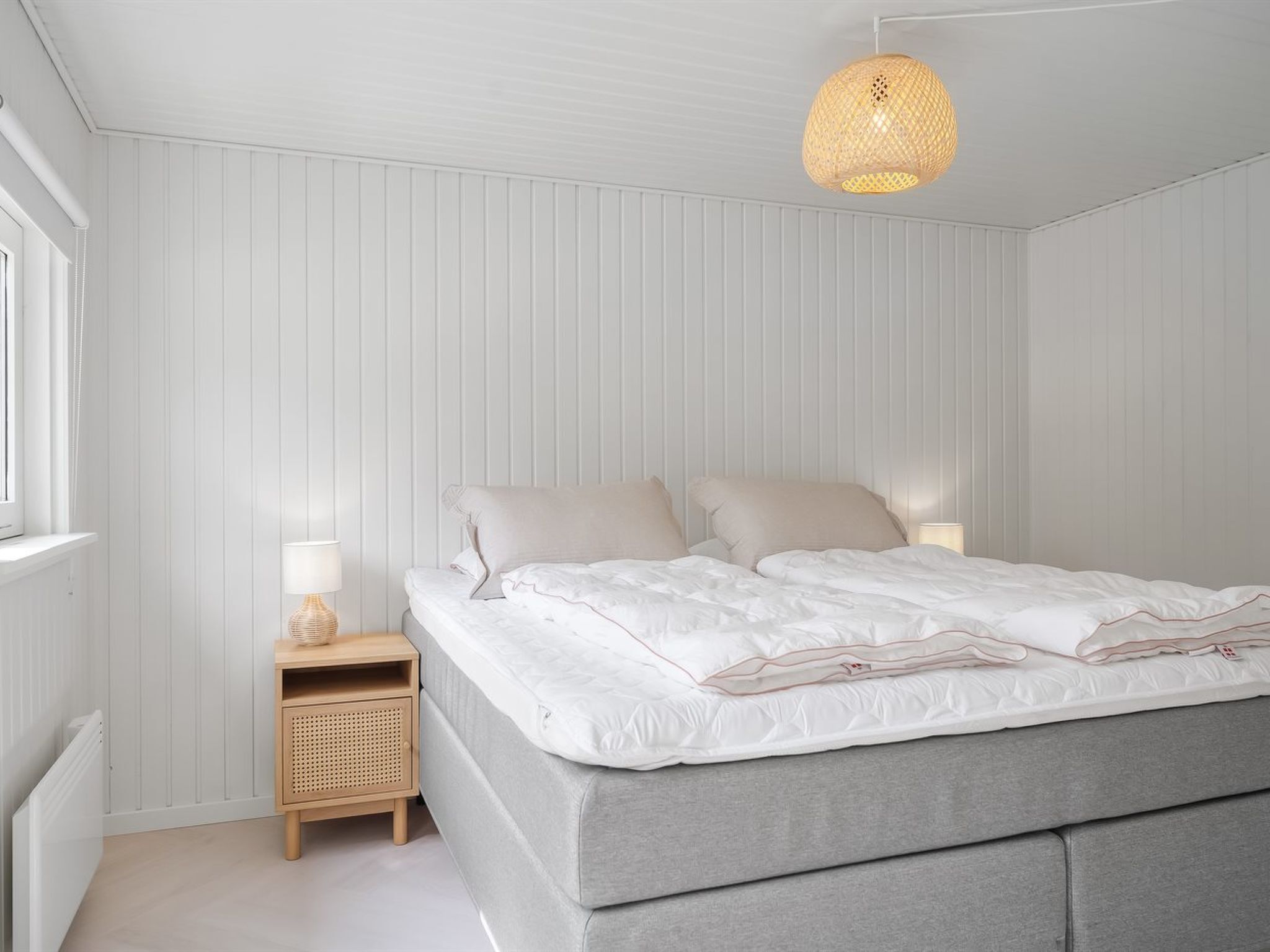 Een slaapkamer met een bed, nachtkastjes, een lamp en een hanglamp.