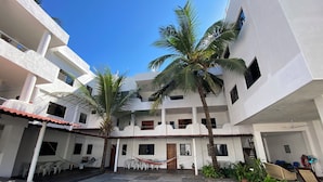 Un patio con suelo de baldosas, edificios blancos, palmeras y mobiliario exterior.