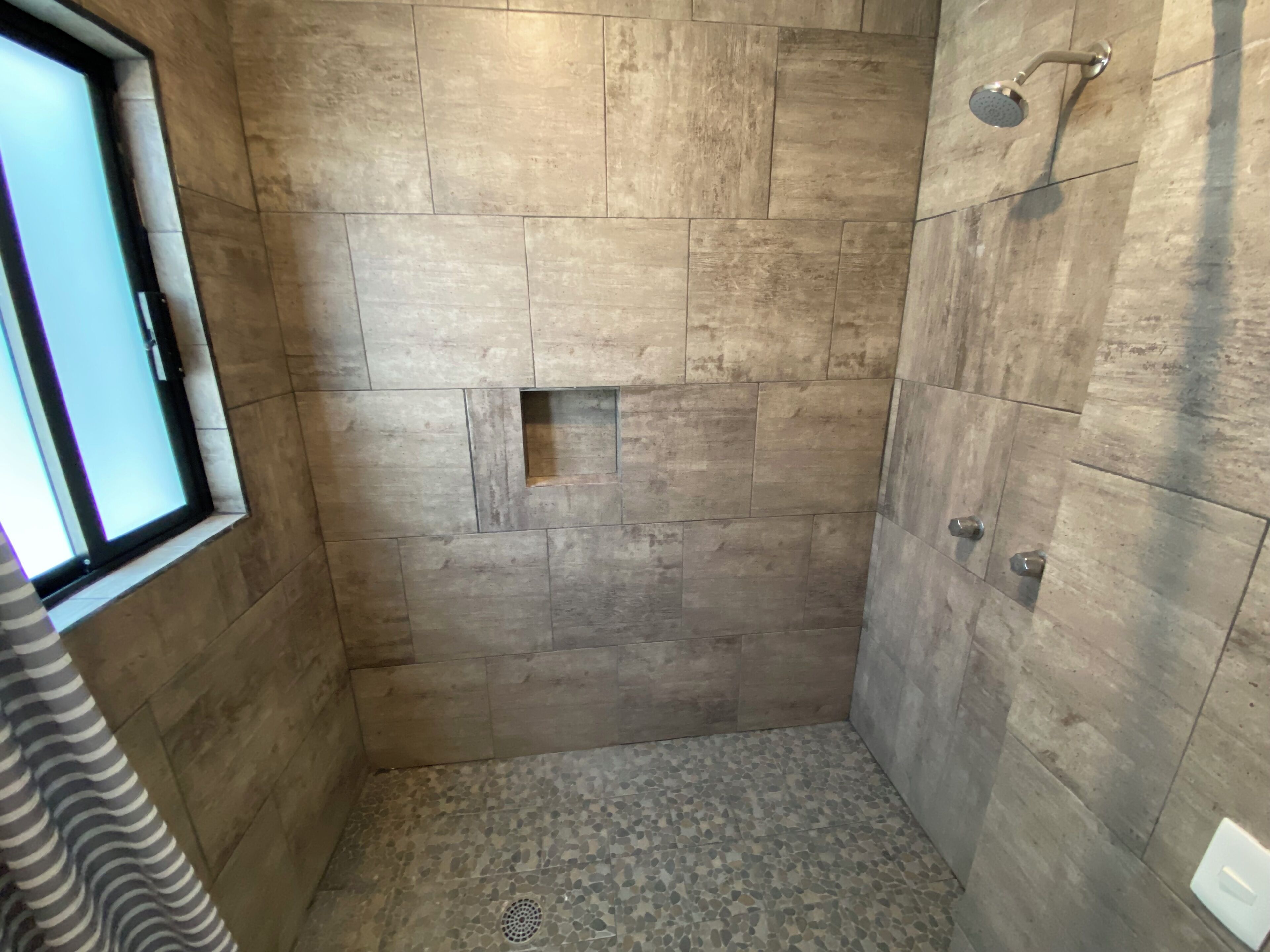 A small, tiled shower room with a window on one side.