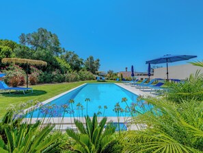 Une piscine rectangulaire à l’eau bleue, entourée d’une pelouse où se trouvent des chaises longues bleues et des parasols.