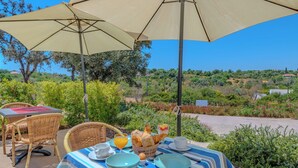 An outdoor dining area with wicker chairs, a table with a striped tablecloth, and a view of the countryside. - Suites Sunny Hill by Interhome (Moncarapacho/Olhão)