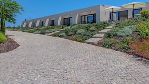 A modern building with a paved pathway leading to a seating area with umbrellas. - Suites Sunny Hill by Interhome (Moncarapacho/Olhão)