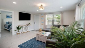 A modern living room with a flat-screen TV, a sofa, a coffee table, and a large plant. - Calm Sea Cottage: New Renovation, Modern 2BR (Bradenton)