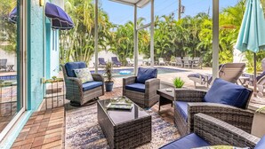 A sunlit patio with wicker furniture, a glass table, and a view of a pool and tropical vegetation. - 2 Villas back to back, 2 Private Heated Pools, New Renovation (Sarasota)