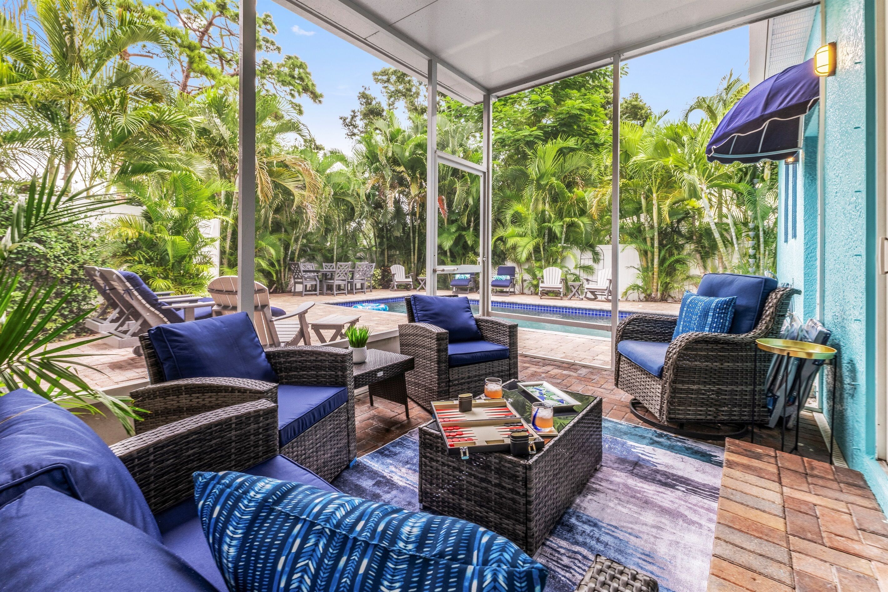 An outdoor patio with wicker furniture, a pool, and lush greenery.