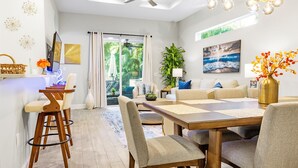A modern living room with a dining area, featuring a ceiling fan, a chandelier, and a large window with curtains. - 2 Villas back to back, 2 Private Heated Pools, New Renovation (Sarasota)