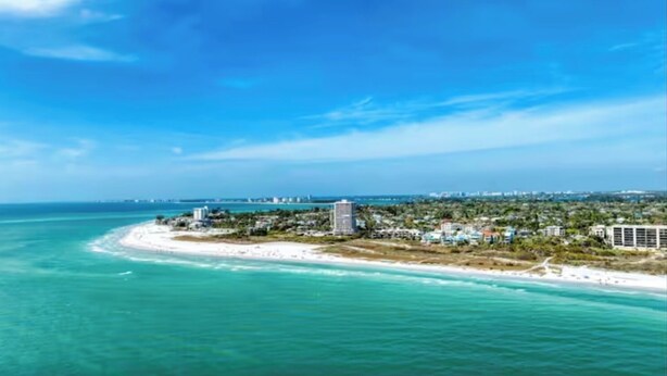 Meeresblick mit Strand, Gebäuden und blauem Himmel.