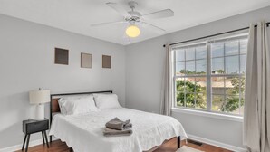 A bedroom with a bed, a nightstand, a ceiling fan, and a large window with curtains. - Lampkin Stay, Cotton District, Walk to MSU (Starkville)