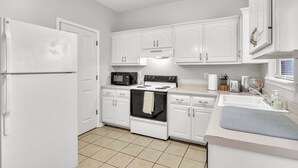 A kitchen with white cabinets, a stove, a microwave, and a sink. - Lampkin Stay, Cotton District, Walk to MSU (Starkville)