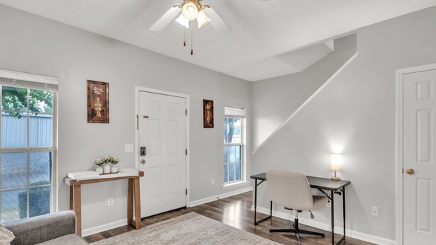 A spacious living room with hardwood floors, a ceiling fan, a sofa, a coffee table, and a desk with a lamp. - Lampkin Stay, Cotton District, Walk to MSU (Starkville)