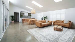 A spacious living area with a modern sofa set, a dining table, and a kitchen in the background. - Large Retreat with Outdoor Living & Kids’ Paradise (Ocean Grove)
