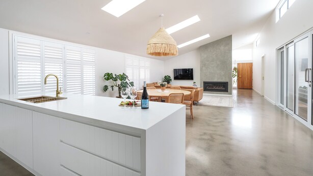 A modern kitchen with a large island, white cabinetry, and a dining area with a round table and chairs. - Large Retreat with Outdoor Living & Kids’ Paradise (Ocean Grove)