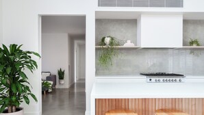A modern kitchen with a white countertop, wooden stools, and potted plants. - Large Retreat with Outdoor Living & Kids’ Paradise (Ocean Grove)
