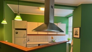 A kitchen with green walls, white cabinets, and a wooden countertop. There is a stainless steel range hood above the stove, and pendant lights hanging above. - Greenbrook Suites (Aalborg)