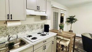 A modern kitchen with white cabinets, a stove, and a sink. There is a dining area with a table and chairs. - Comfort Suite in charming Bay Shore (Bay Shore)