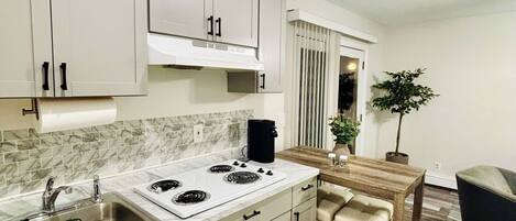 Una cocina moderna con armarios blancos, una estufa y un fregadero. Hay un comedor con una mesa y sillas.