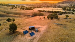 A rural landscape with a small house, solar panels, and sparse vegetation. - Gunyah by Tiny Away (Wyangala)