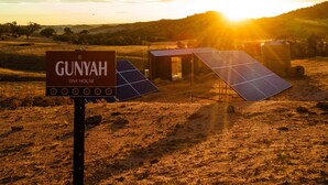 A sign for 'GUNYAH TINY HOUSE' with solar panels and a small building in a rural landscape. - Gunyah by Tiny Away (Wyangala)