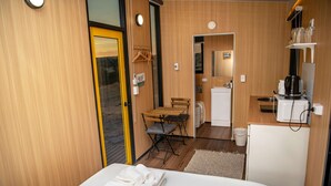 A compact room with a bed, a small table, a chair, a kitchenette, and a door leading outside. - Gunyah by Tiny Away (Wyangala)