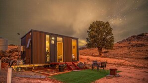 A modern cabin with a glass door, a small outdoor seating area, and a starry night sky. - Gunyah by Tiny Away (Wyangala)