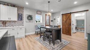 Une cuisine avec des meubles blancs, une table à manger avec des chaises, un lustre et une porte en bois de style grange.
