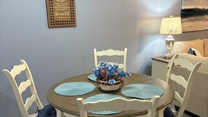 A dining area with a round table, white chairs, and a decorative wall piece.