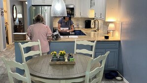 A modern kitchen with white cabinets, a dining table with chairs, and a hanging pendant light.