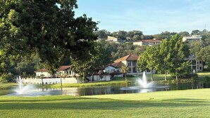 A golf course with a pond, fountains, and houses in the background.