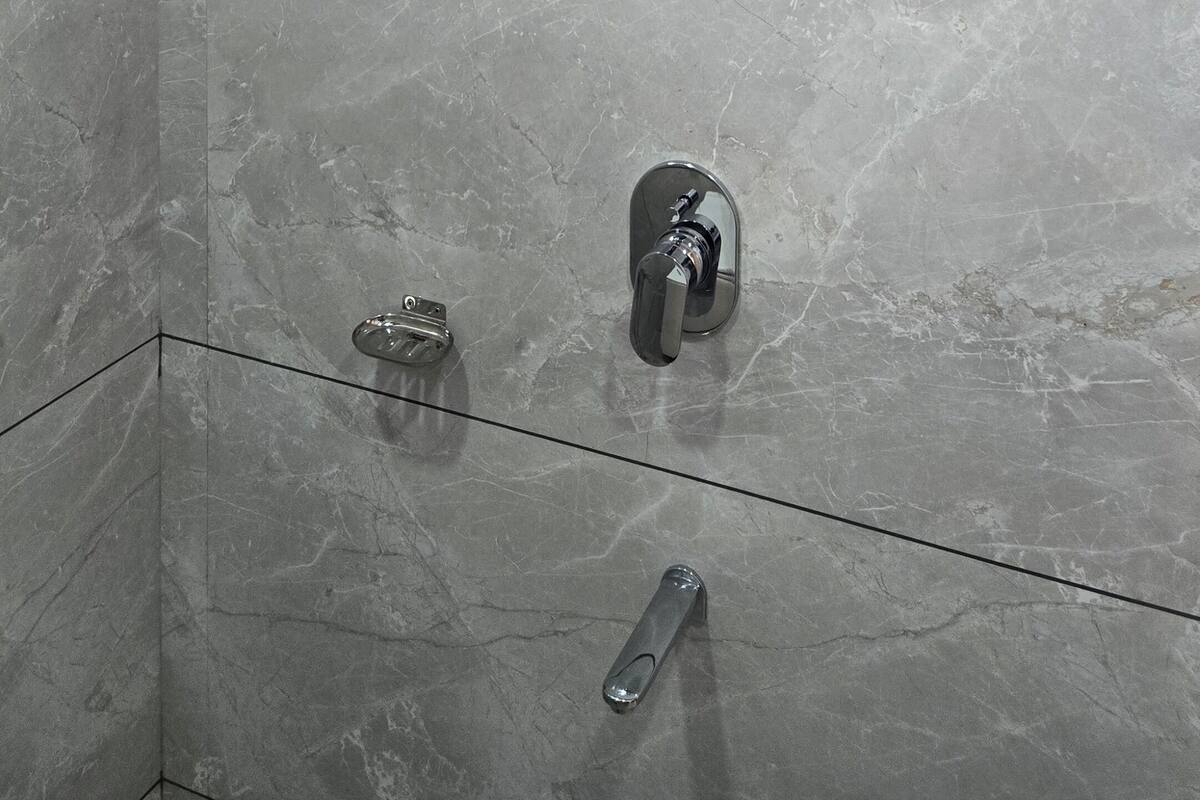 A tiled shower area with a handheld showerhead, a wall-mounted faucet, and a ceiling-mounted showerhead.
